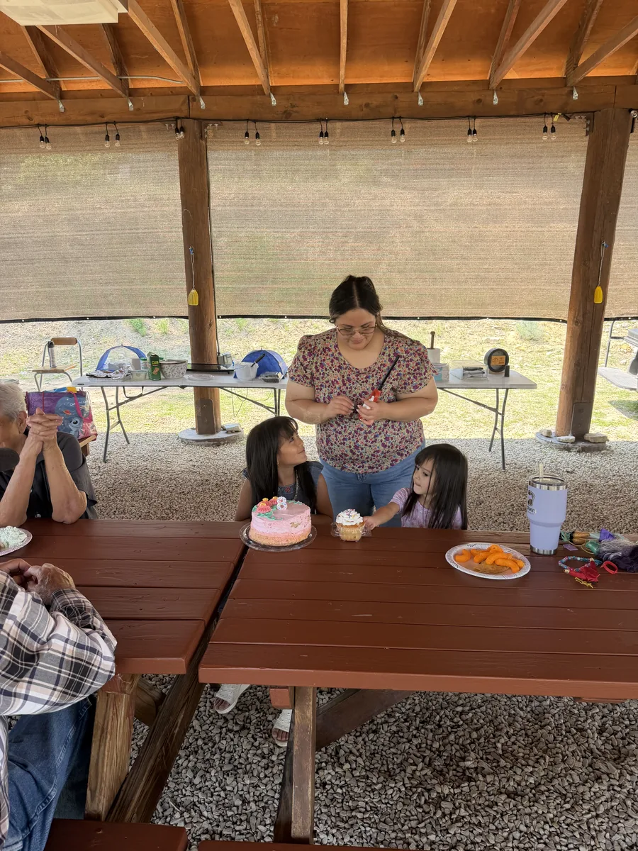 A birthday cake on the pavilion table with the family gathered around