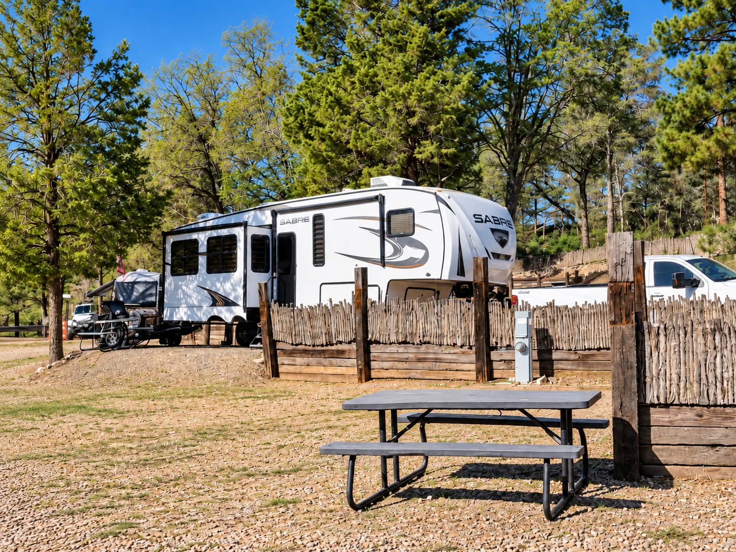 A Sabre travel trailer on a terraced gravel site with a picnic table in the pines
