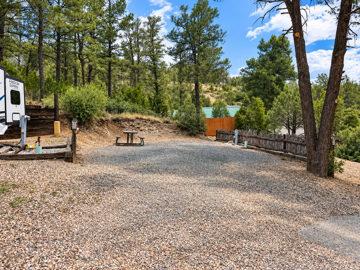 A wide gravel RV site with a picnic table beneath tall Ruidoso pines